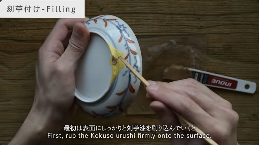 Fill gaps and missing areas with clay-lacquer paste — A small hera presses the clay-lacquer filler into a chipped loss on the ceramic edge.