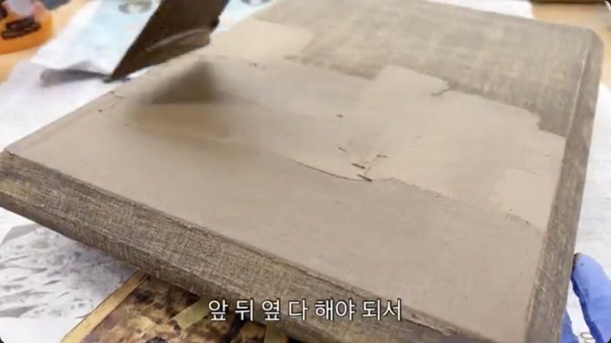 Mix and apply the first ground coat (sabi / tohwachil) — A broad hera spreads the first ground coat across the reinforced panel in a thin, continuous layer.